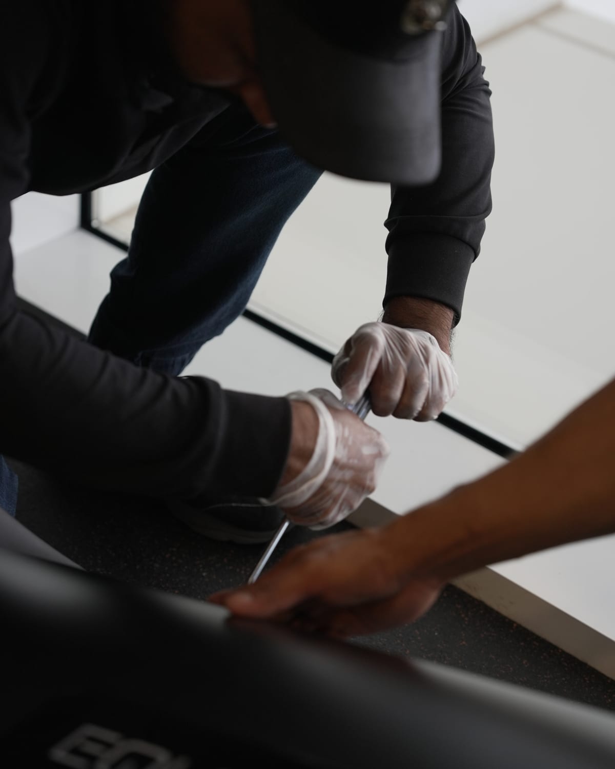 An Equipt engineer working on the rail of a treadmill deck with a hand tool.